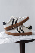 Pair of white sneakers with black stripes and brown soles on a gray background