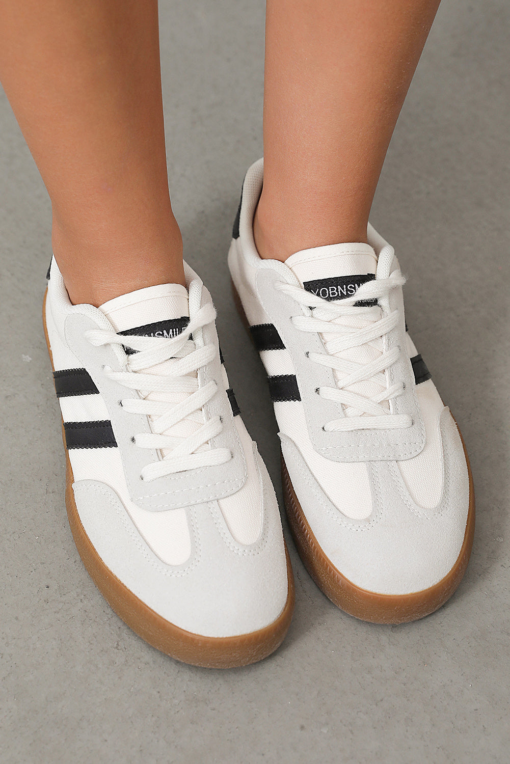 White sneakers with black stripes and brown soles on a neutral background