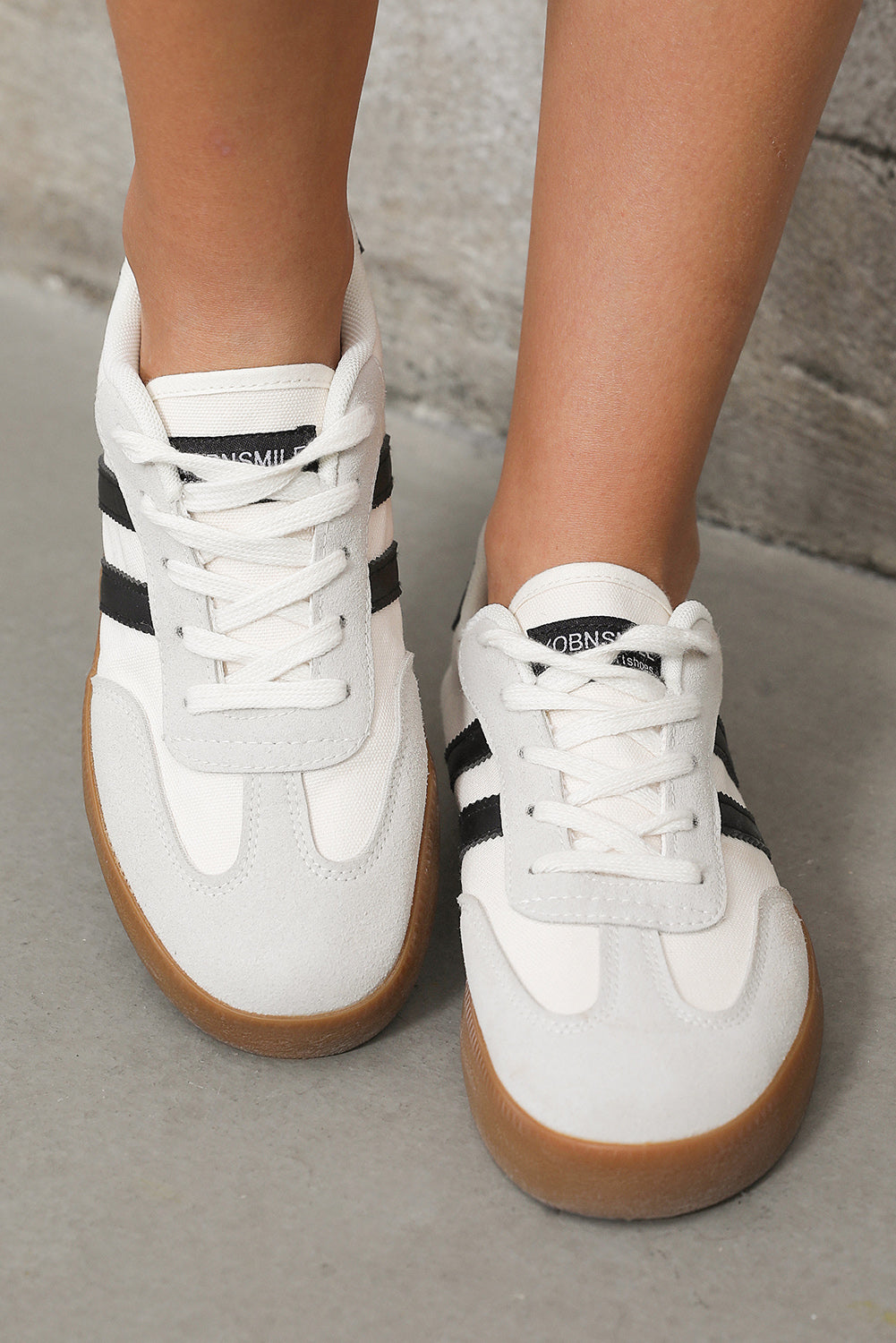 White sneakers with black stripes and brown soles on a neutral background