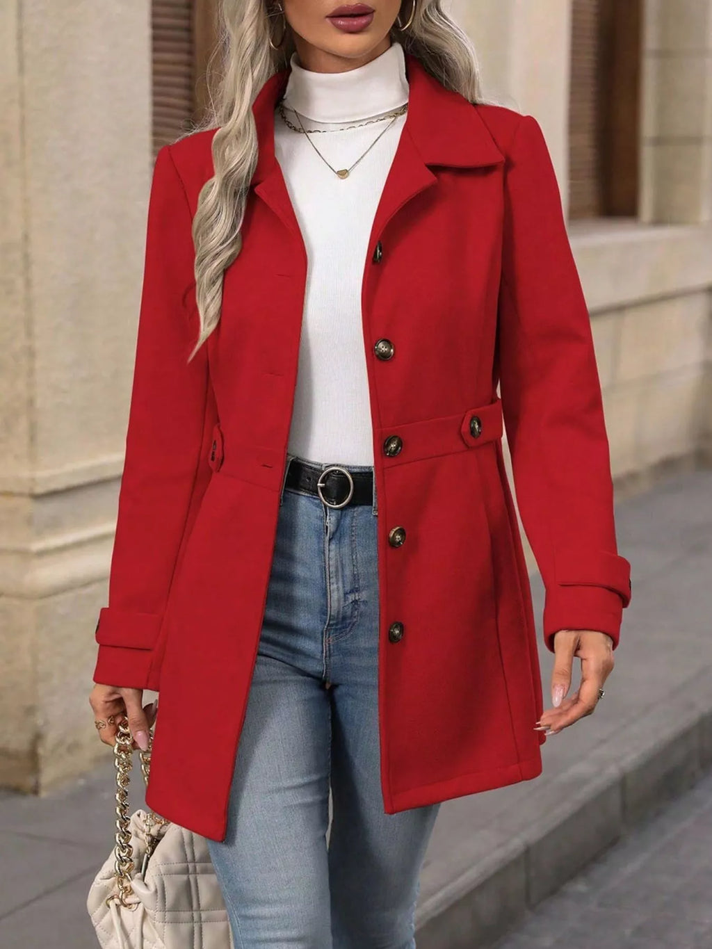 Person wearing a red coat over a white top and blue jeans, standing against a neutral background.