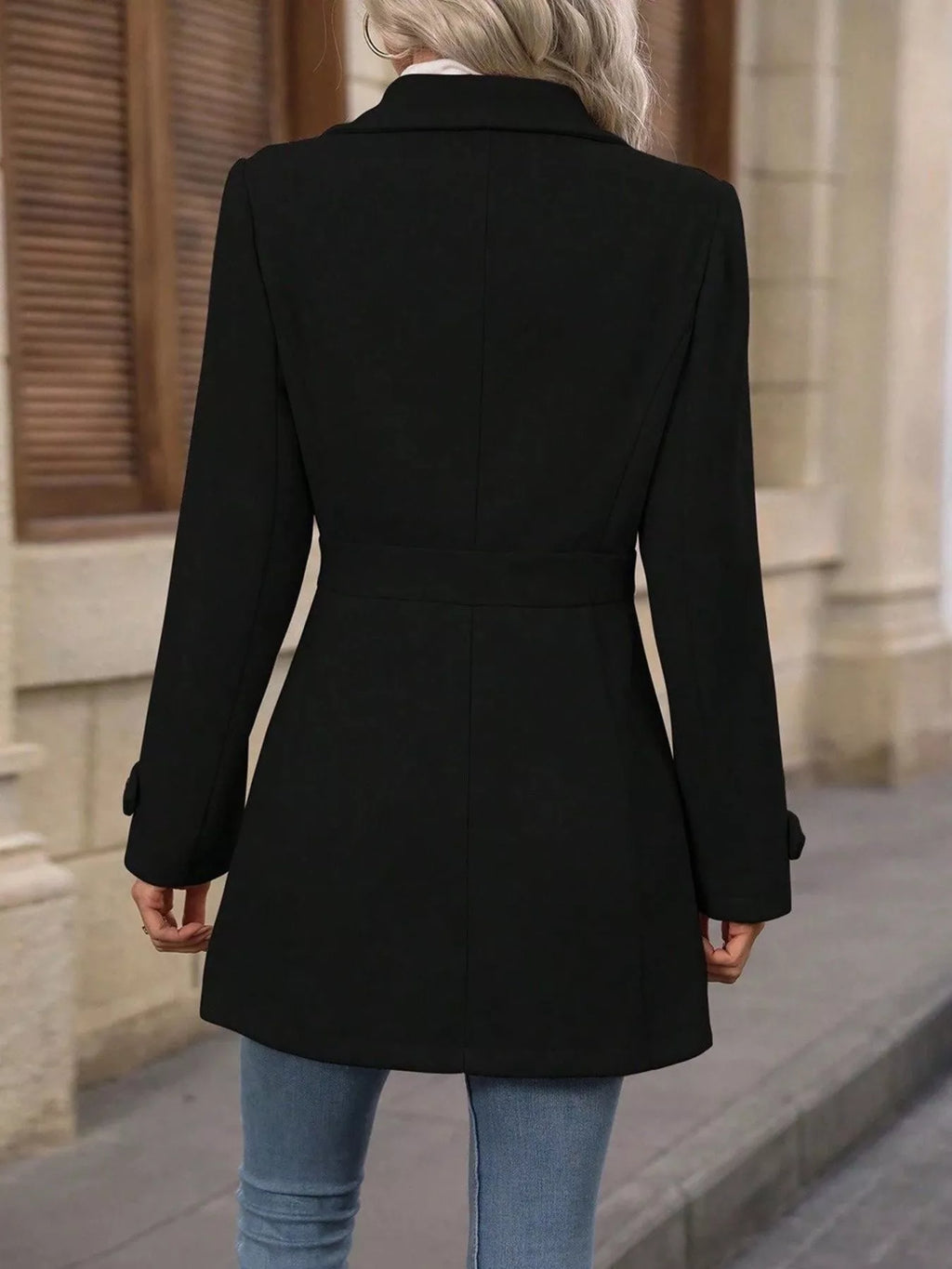 Person wearing a black coat and blue jeans standing on a street.