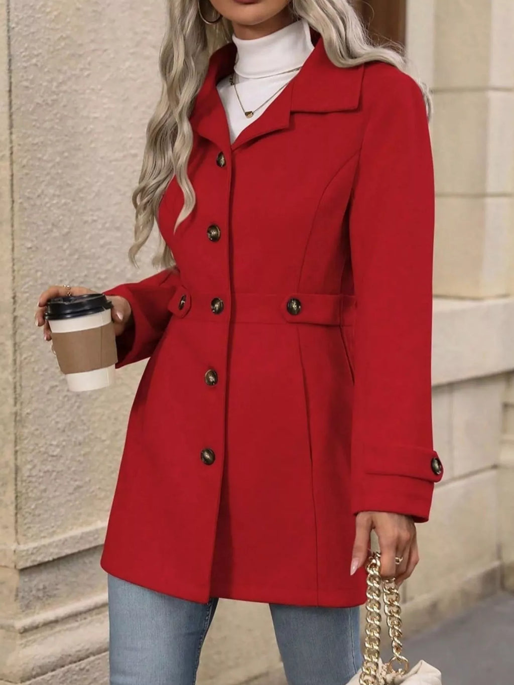 Person wearing a red coat holding a coffee cup against a neutral background