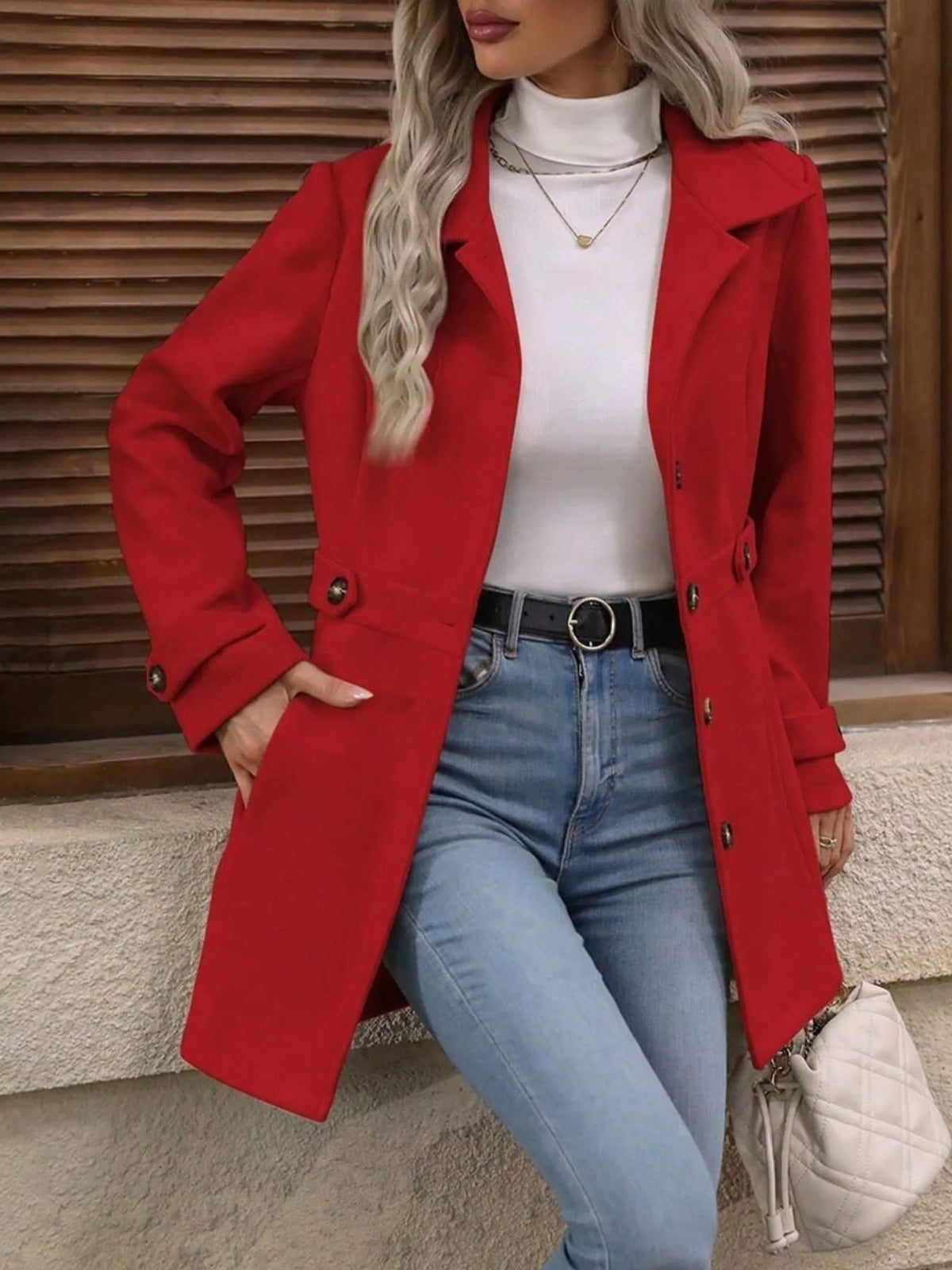 Person wearing a red coat over a white top and blue jeans, sitting against a wooden panel background.