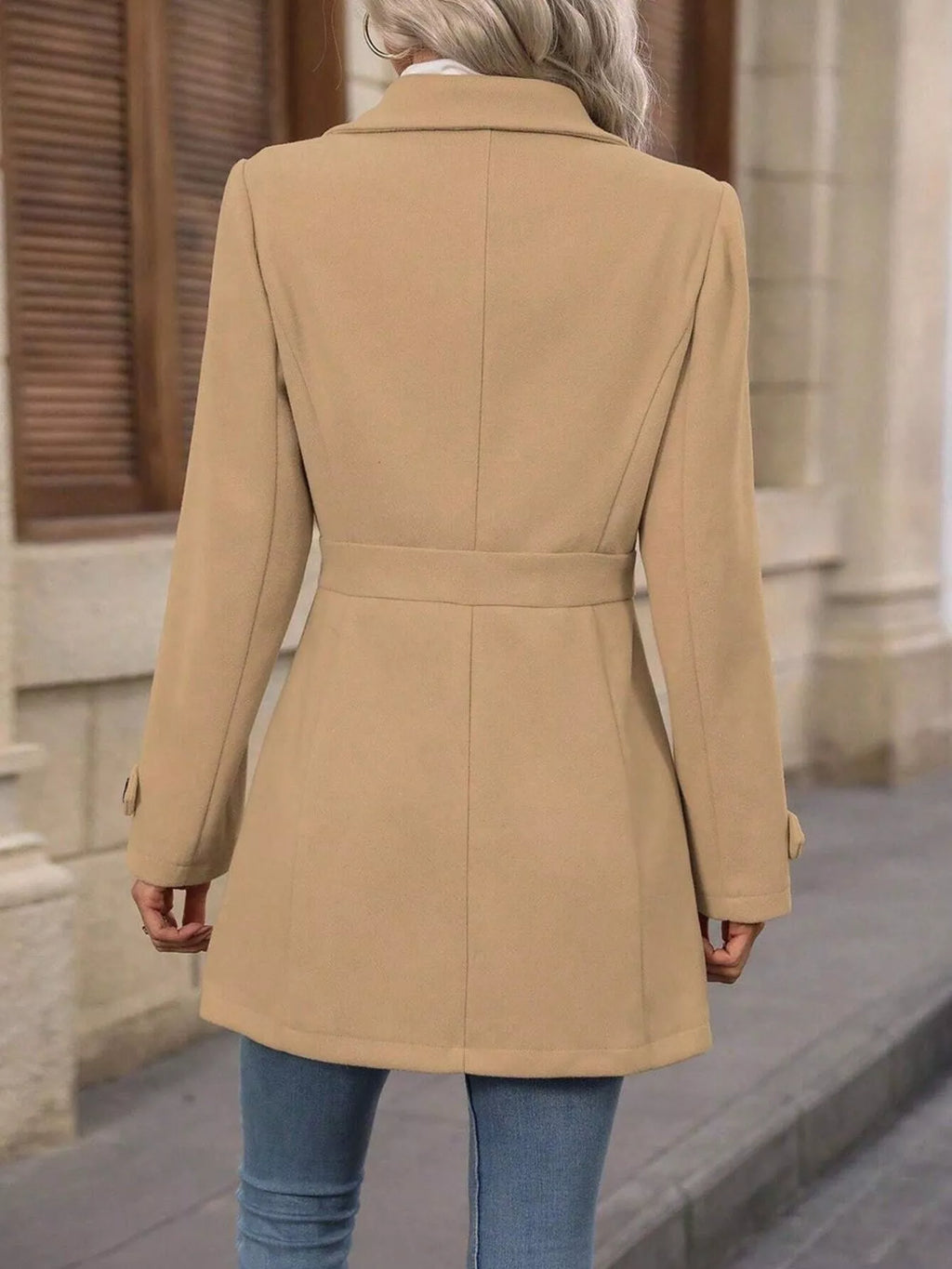 Person wearing a beige coat walking on a street.