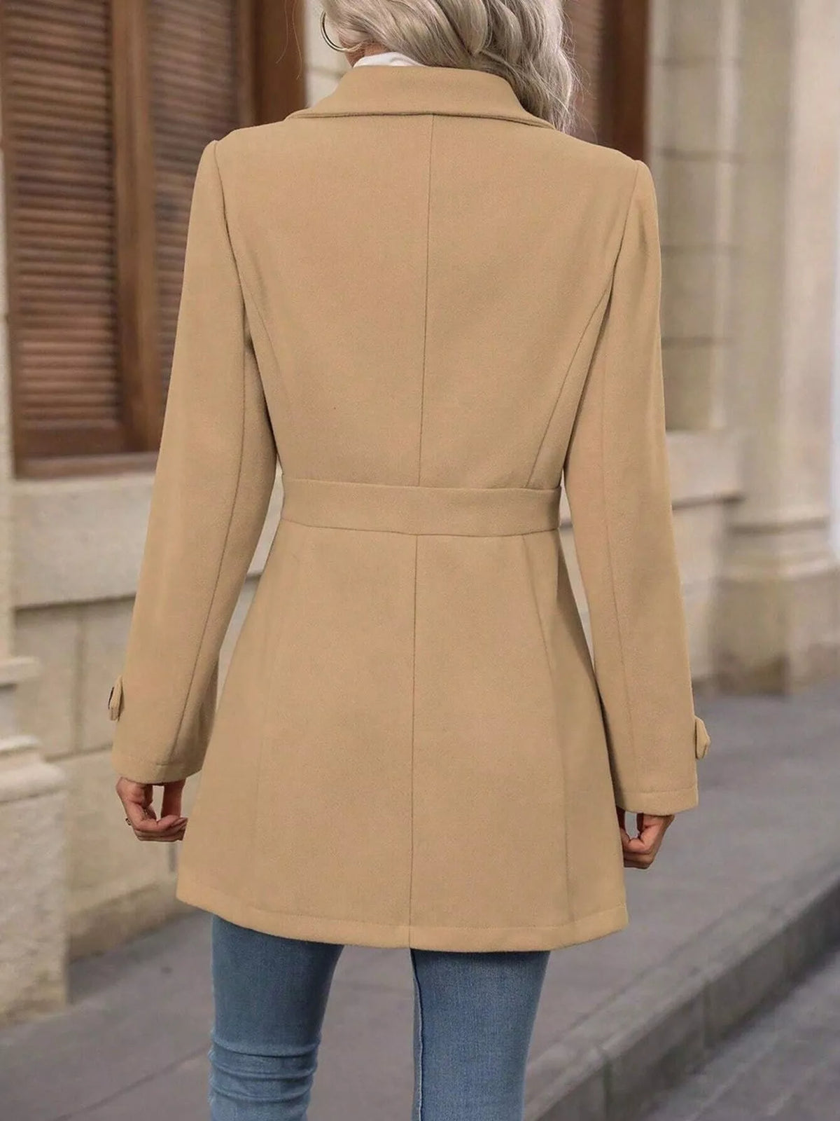Person wearing a beige coat walking on a street.