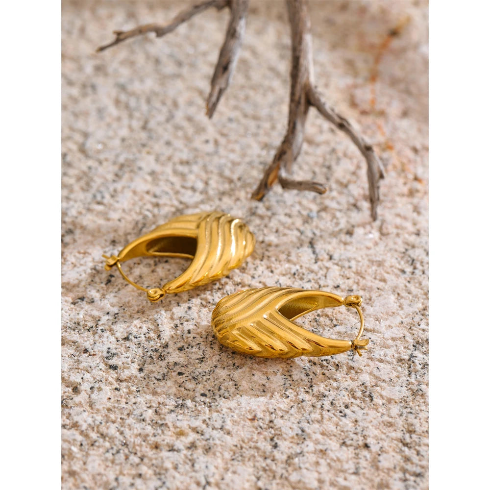 Gold hoop earrings on a sandy surface with driftwood.