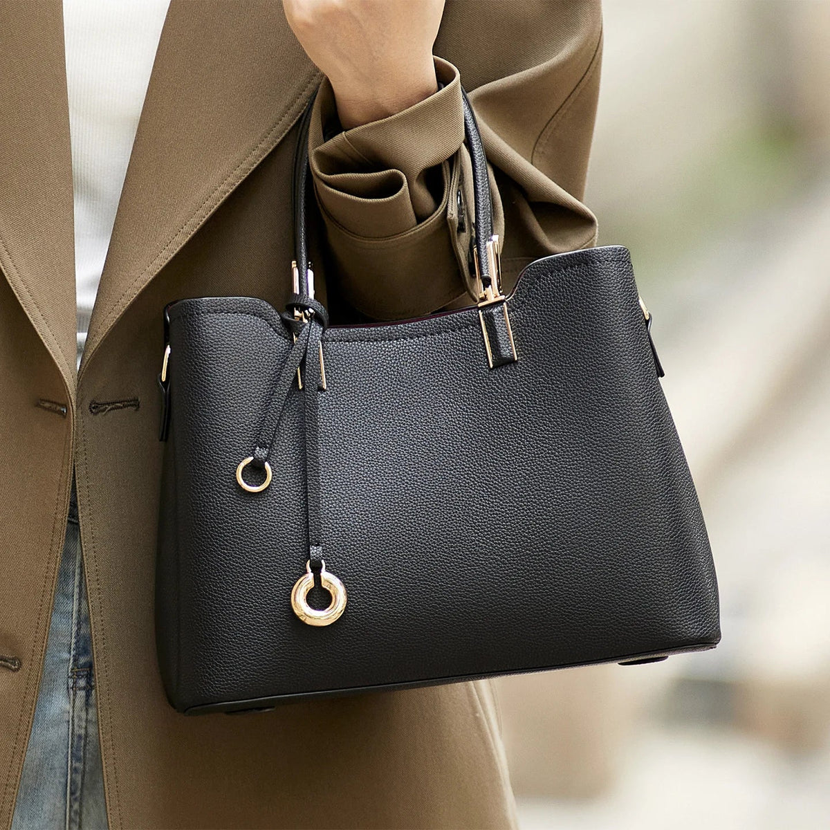 Black handbag with gold accents held by a person wearing a brown coat.