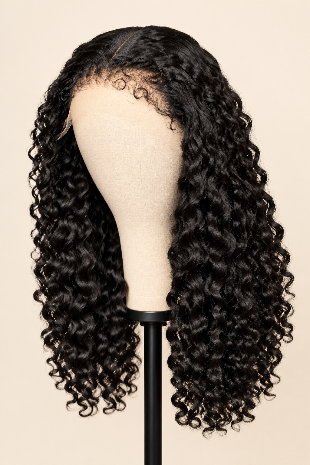Black curly wig with deep waves displayed on a beige mannequin head stand against a solid beige background.