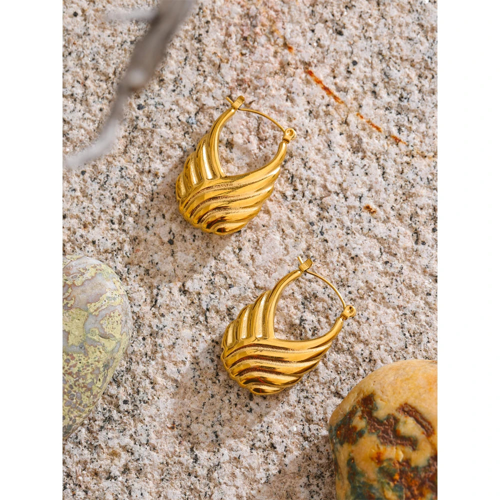 Gold hoop earrings on a textured surface with stones