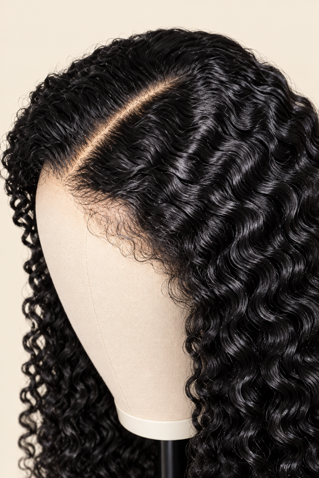 A close-up of a black curly wig displayed on a mannequin head against a light beige background. The wig features deep, glossy curls with a natural-looking lace part line.
