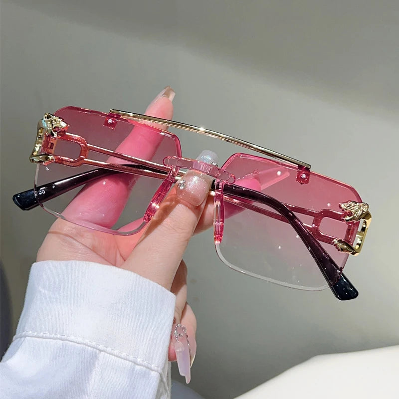 Pink sunglasses with gold accents held by a hand against a neutral background