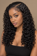 A woman with long, glossy, deep curly hair wearing a black strapless top, photographed against a solid warm beige background.