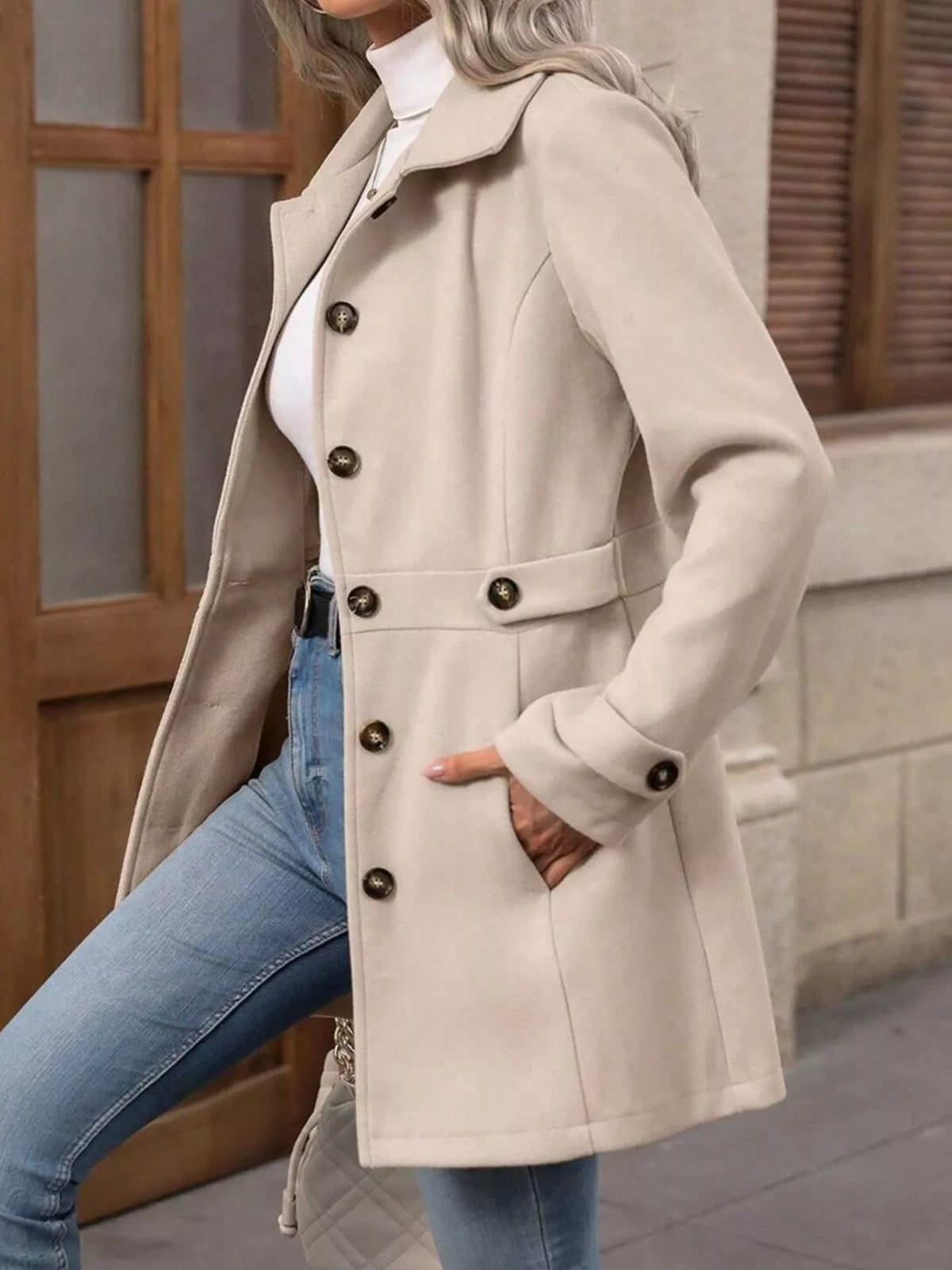 Person wearing a beige coat with button details, standing against a neutral background.