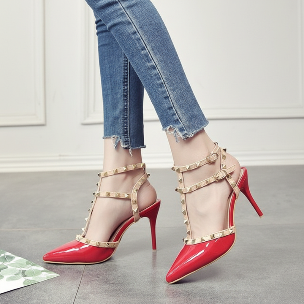 Red high-heeled shoes with gold straps worn with blue jeans on a light wooden floor.