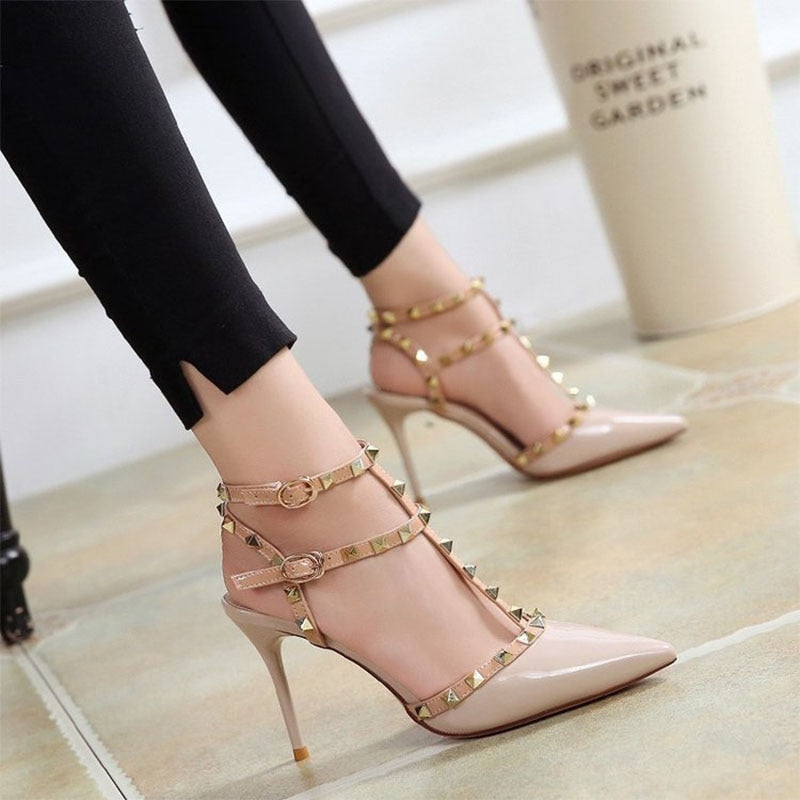 High-heeled shoes with studded details worn by a person on a light wooden floor.