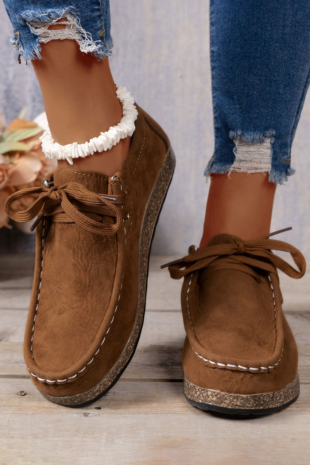 Brown suede shoes with lace-up design worn with ripped jeans on a wooden floor.