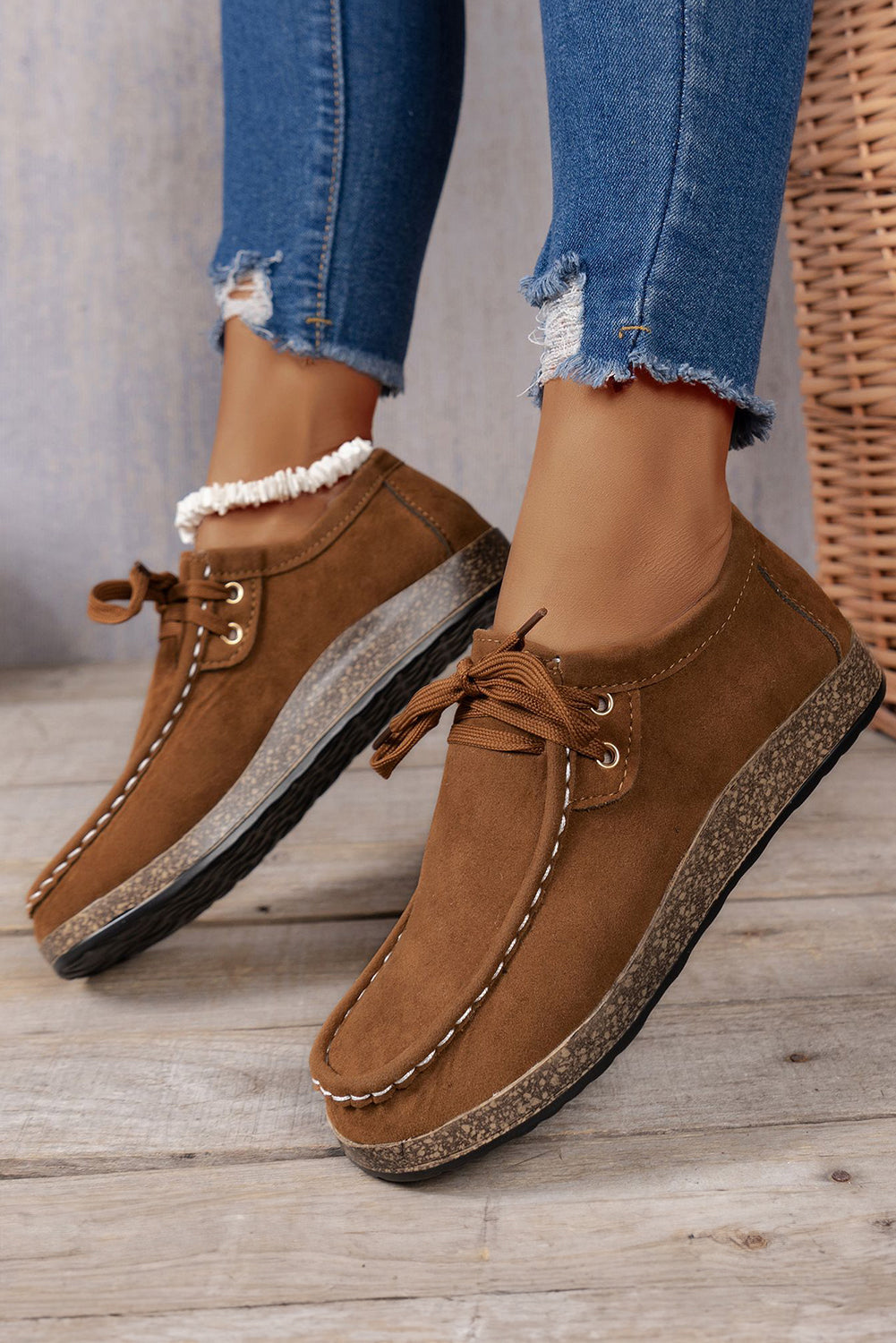 Brown loafers with white laces worn with blue jeans on a wooden floor.