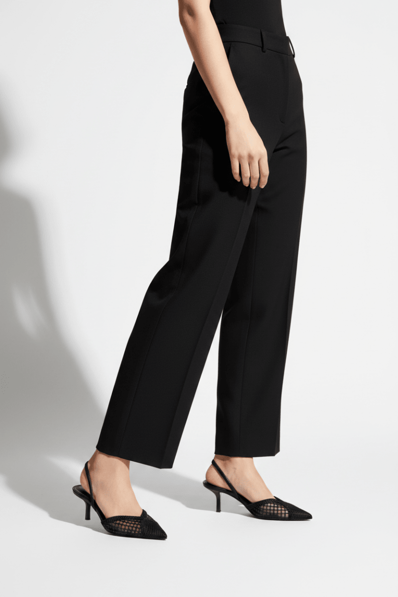 Person wearing black high-waisted pants and black high-heeled shoes on a white background