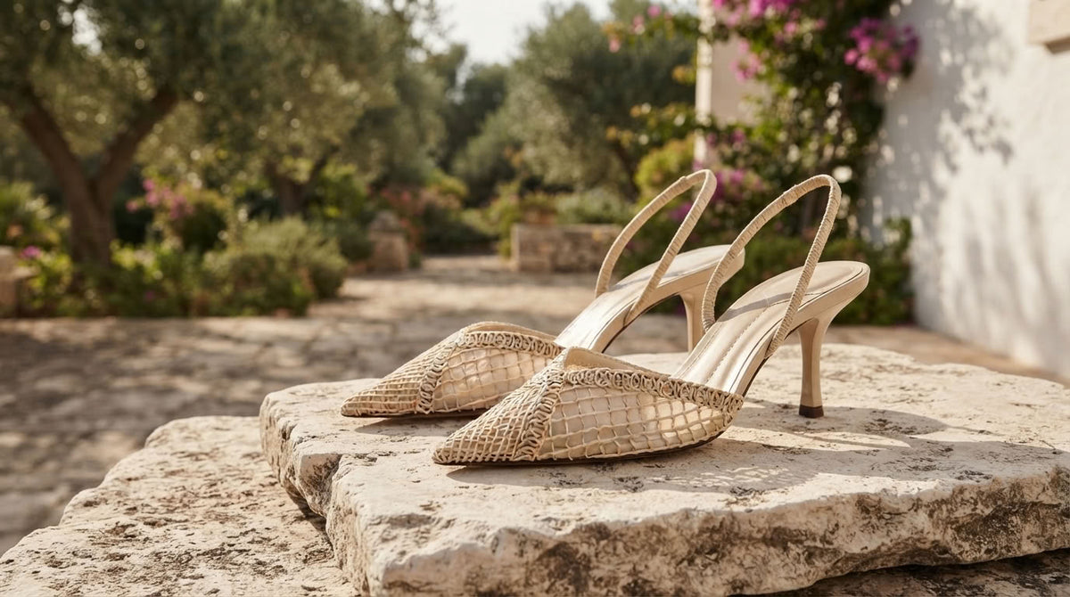 A pair of beige pointed-toe slingback heels with a textured snakeskin pattern, resting on a rustic stone slab in an outdoor garden setting.