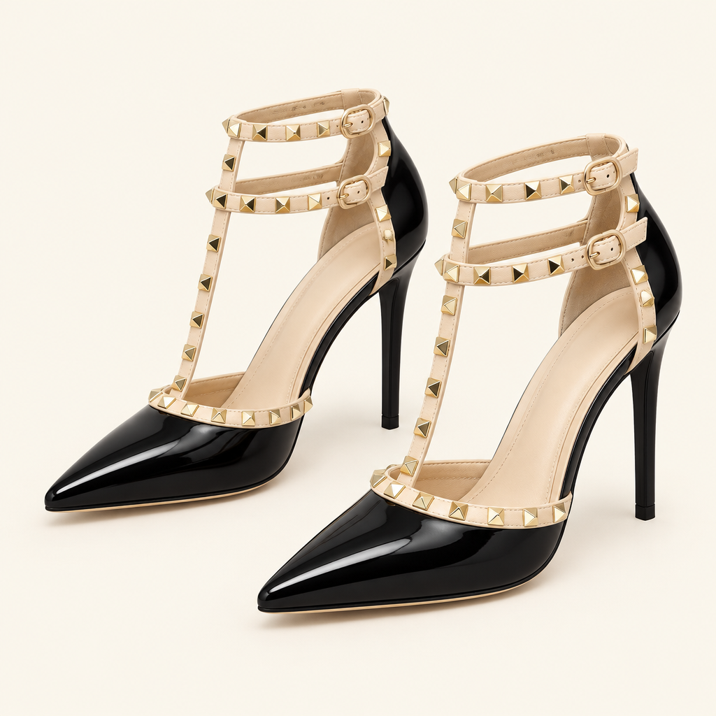 A pair of black patent pointed-toe high heels with beige ankle straps and gold pyramid studs, shown on a light cream background.