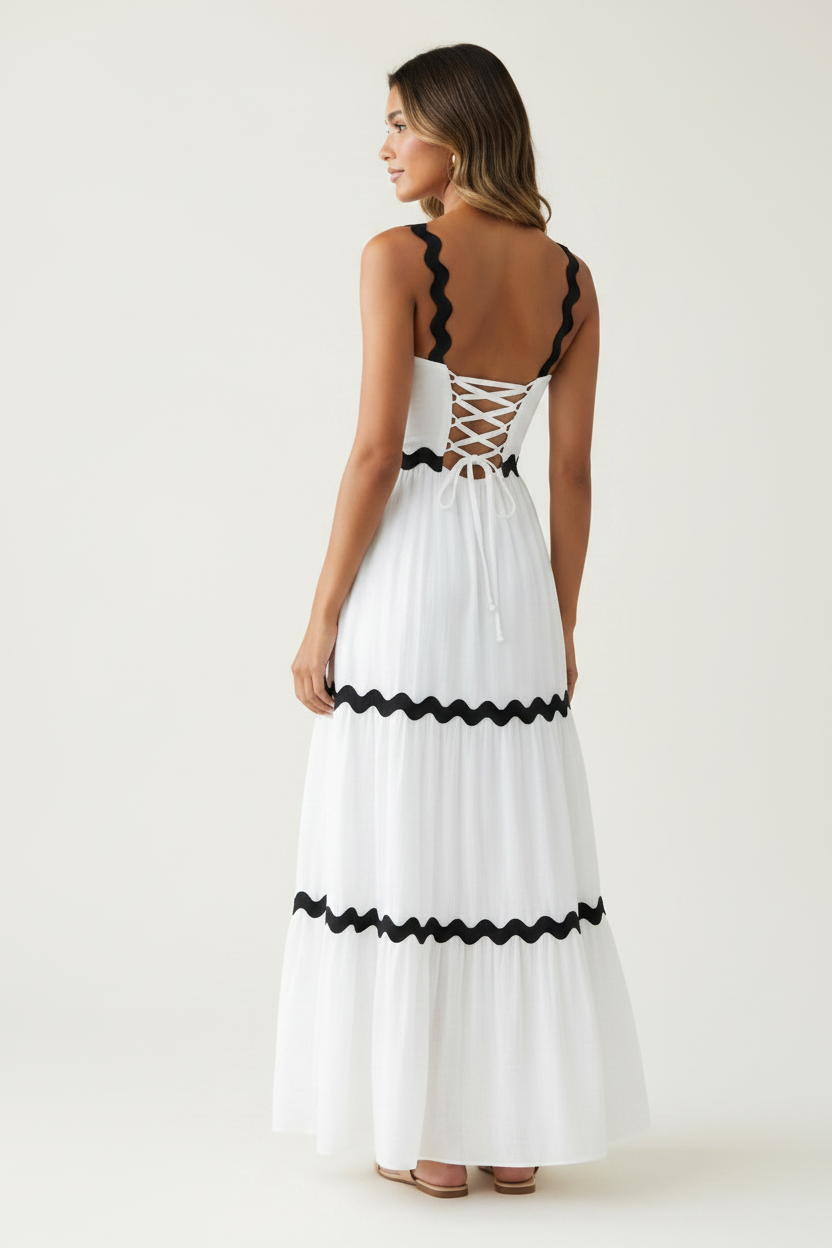 Back view of a model wearing a white tiered maxi dress with a lace-up back and scalloped trim