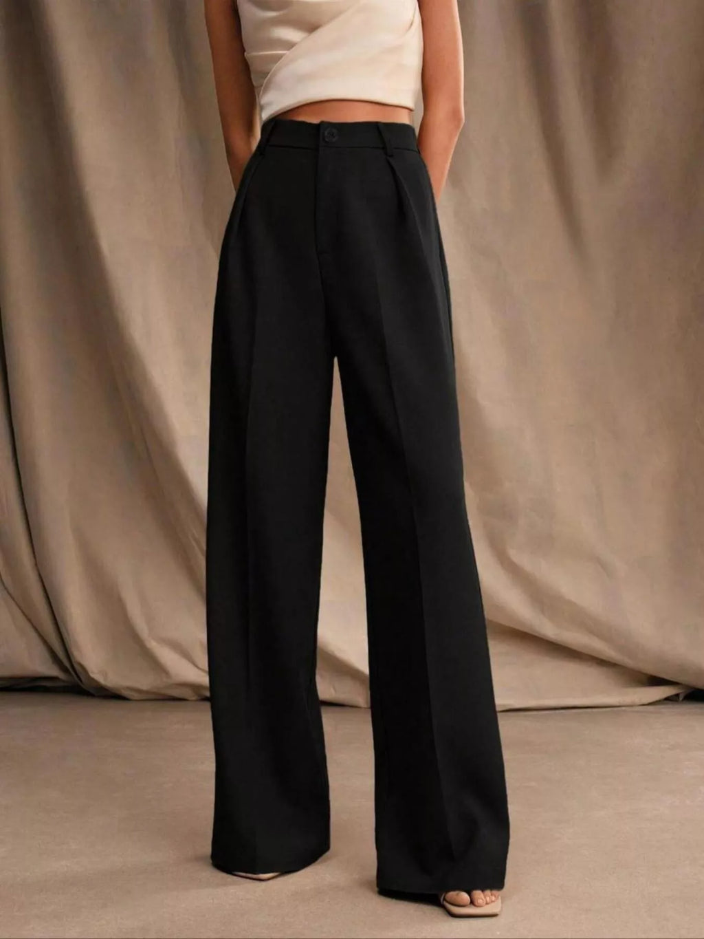 Person wearing black wide-leg pants against a beige curtain background